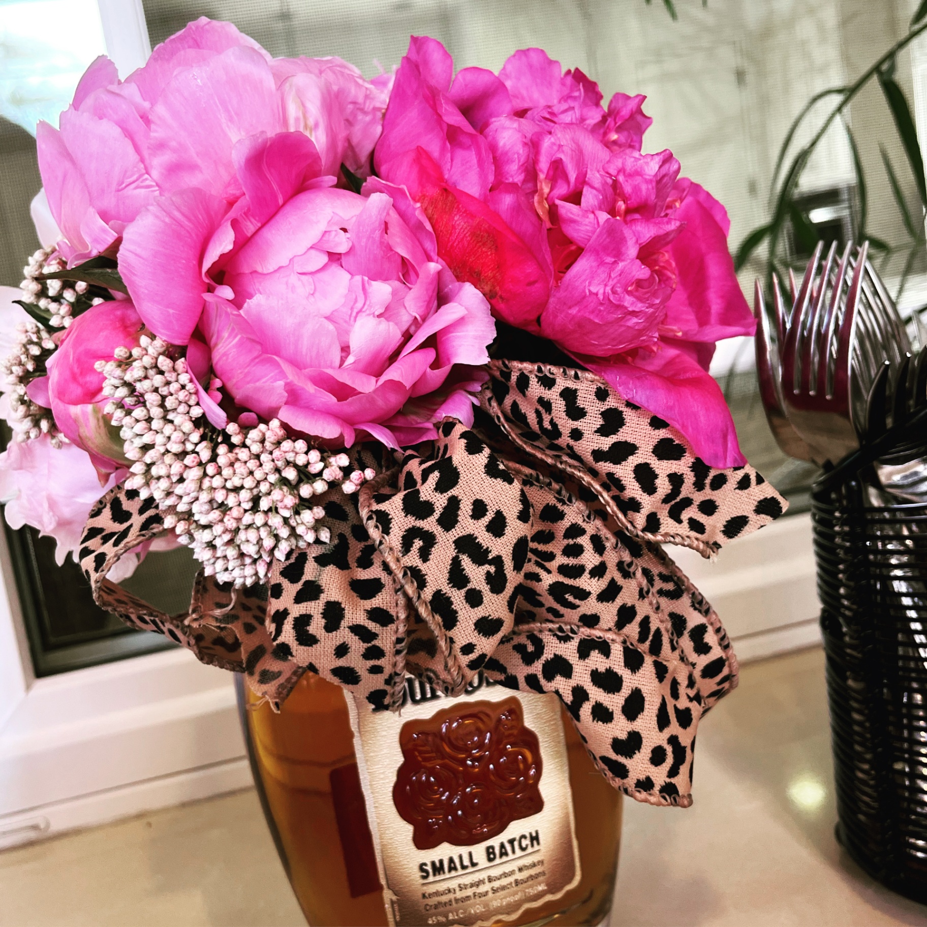 Pink peonies in a bourbon bottle with leopard ribbon